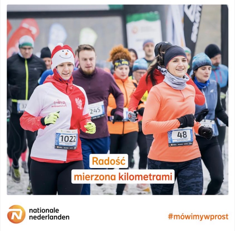 Grupa biegaczy podczas zimowego maratonu, z numerami startowymi i uśmiechniętymi twarzami, sponsorowana przez Nationale Nederlanden.