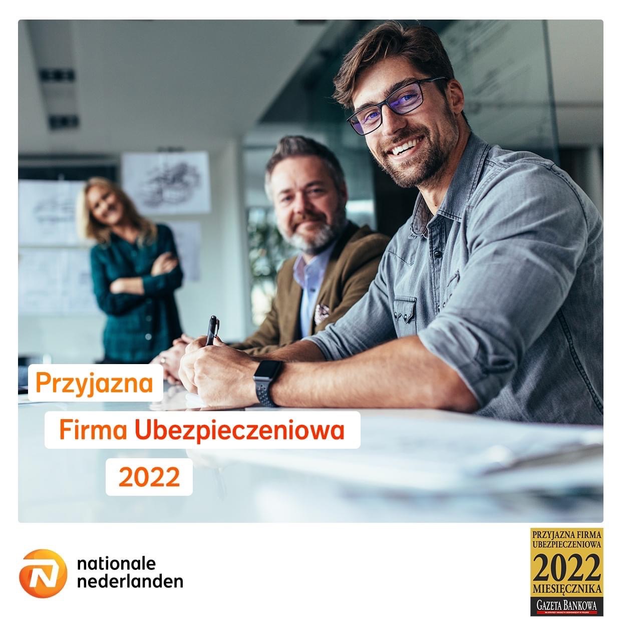 Trzech uśmiechniętych pracowników firmy podczas spotkania, mężczyzna w okularach na pierwszym planie trzyma długopis nad dokumentami.