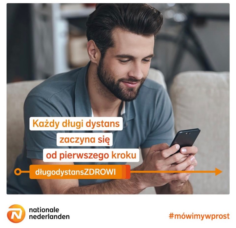 Mężczyzna z brodą przegląda smartfon siedząc na kanapie; grafika z hasłem 'Każdy długi dystans zaczyna się od pierwszego kroku' i logo Nationale Nederlanden.