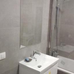 Przemek Łodożyński - Szara łazienka z umywalką na szafce z dwiema szufladami, lustrem i kabiną prysznicową z widoczną baterią. Na umywalce leży mydło w mydelniczce.