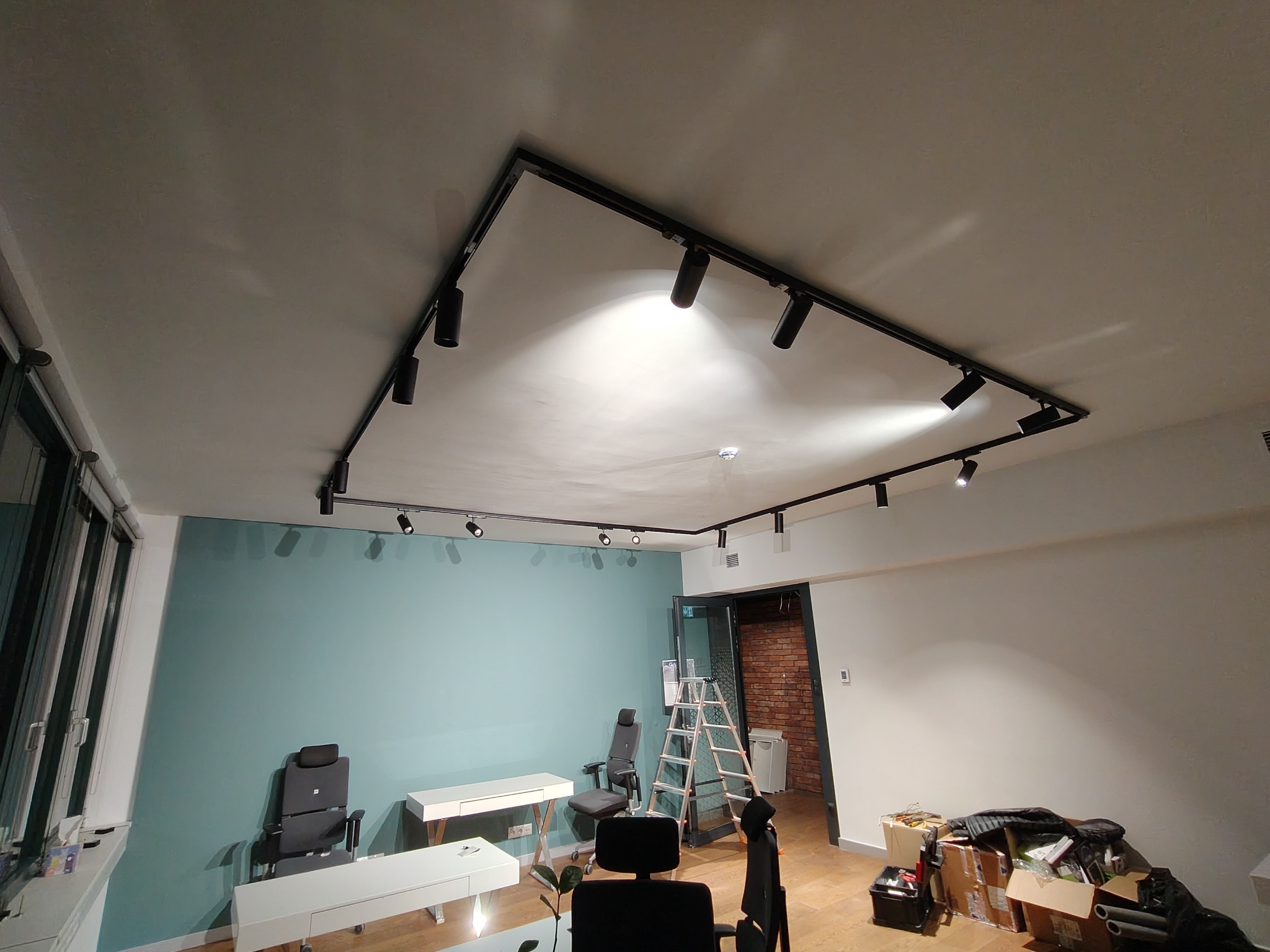 Czarna, szynowa instalacja oświetleniowa z reflektorami punktowymi, zamontowana pod sufitem w nowoczesnym biurze z błękitną ścianą.