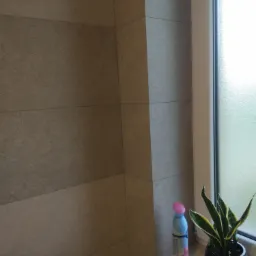 Beżowe płytki wielkoformatowe na ścianie w łazience w Wierzawicach, widok z bliska na fragment ściany, parapet z kwiatem doniczkowym i odświeżaczem powietrza.