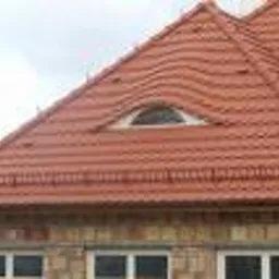 Czerwony dach z dachówki ceramicznej z oknem w kształcie półksiężyca, widok z dołu na fragment budynku w trakcie budowy.