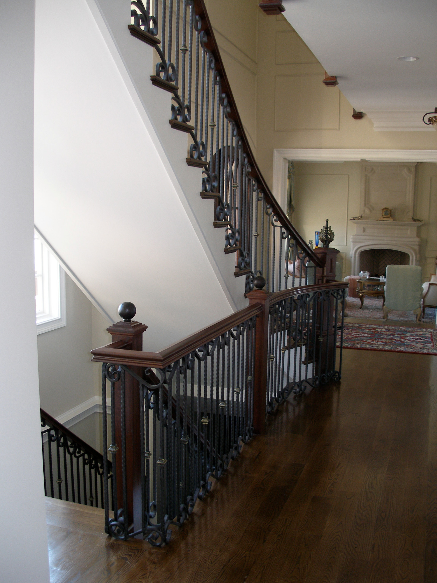 Eleganckie schody z ciemnego drewna z kutymi, czarnymi balustradami, widok z góry na dół z salonem w tle.