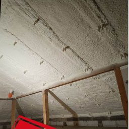 DSH izolacje - Poddasze po aplikacji pianki PUR, widoczne krokwie i równomierna warstwa izolacji. Biała, porowata struktura pianki wypełnia przestrzeń między elementami konstrukcyjnymi.