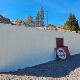 DSH izolacje - Izolacja przeciwwilgociowa fundamentów pianką PUR w Błażowej. Ściana budynku zabezpieczona pianą, widoczne wykopane fundamenty i gruz.