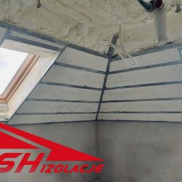 DSH izolacje - Poddasze z oknami dachowymi po izolacji pianką PUR, widoczne metalowe profile i fragment instalacji. Logo firmy w lewym dolnym rogu.