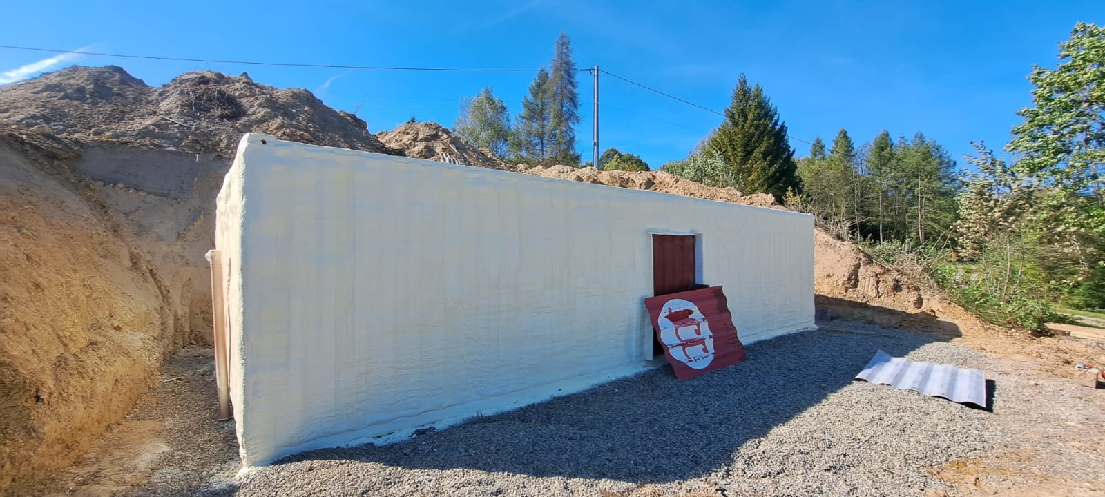 Izolacja przeciwwilgociowa fundamentów pianką PUR w Błażowej. Ściana budynku zabezpieczona pianą, widoczne wykopane fundamenty i gruz.