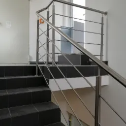 Nowoczesne schody z ciemnymi płytkami i balustradą ze stali nierdzewnej z poziomymi prętami, widok z dołu na górę, minimalistyczny design.