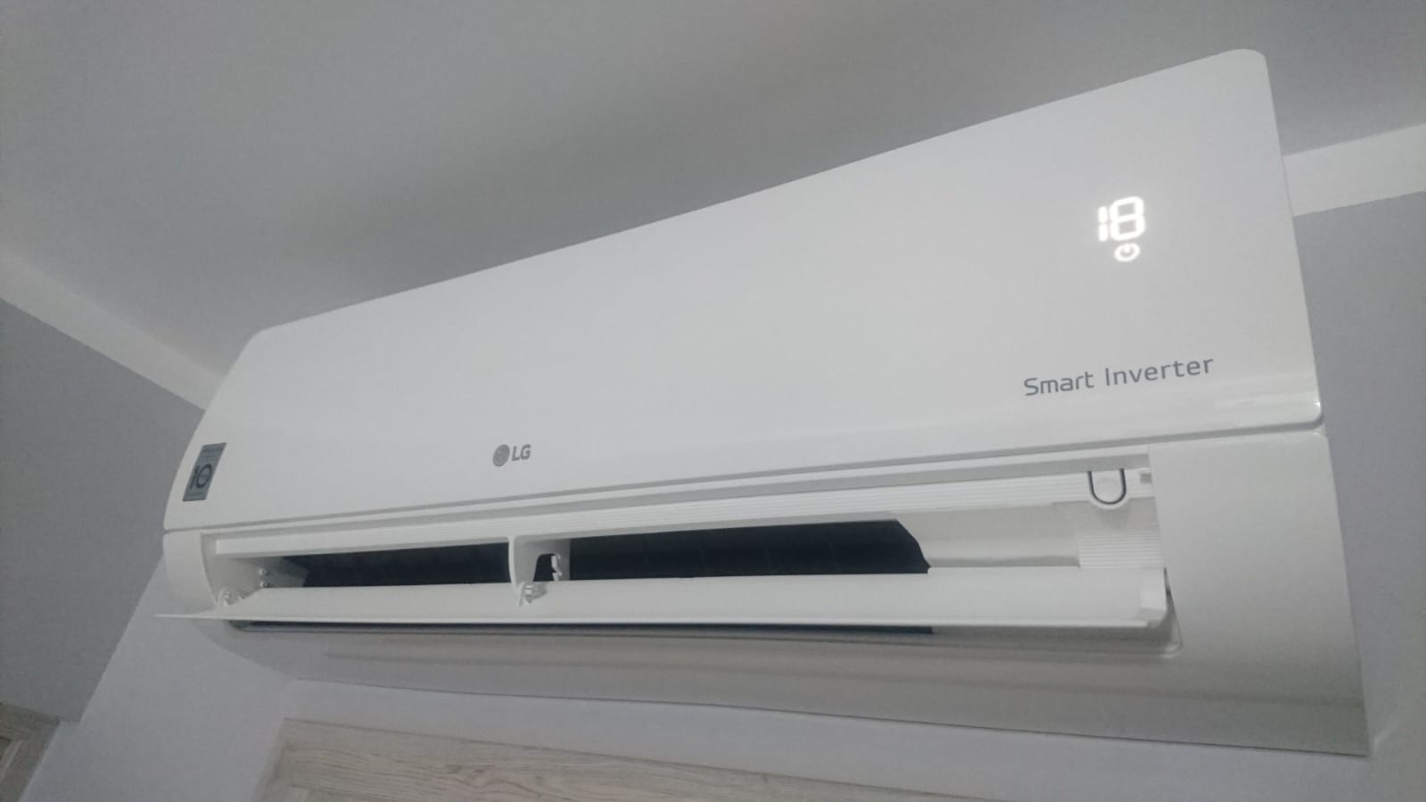 Biała jednostka klimatyzacji LG Smart Inverter zamontowana na ścianie, ustawiona na temperaturę 18 stopni Celsjusza.