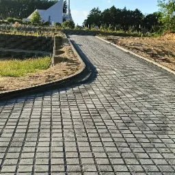 Ułożona szara kostka brukowa prowadząca do nowoczesnego budynku sakralnego na tle błękitnego nieba