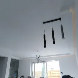 Nowoczesne oświetlenie sufitowe: trzy cylindryczne lampy wiszące na tle białego sufitu i ściany z delikatnym oświetleniem LED wzdłuż krawędzi.