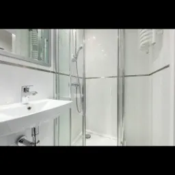 Nowoczesna łazienka z kabiną prysznicową ze szklanymi drzwiami, białą umywalką i grzejnikiem drabinkowym na białych kafelkach z szarymi paskami.