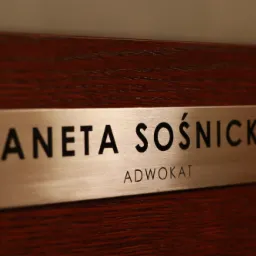 Tabliczka z nazwiskiem Aneta Sośnicka i napisem Adwokat, zamontowana na drewnianej powierzchni.