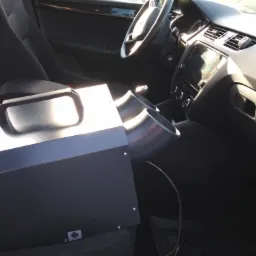 Czarna maszyna z dwoma wylotami powietrza umieszczona na siedzeniu samochodu, prawdopodobnie do odkażania lub odgrzybiania klimatyzacji.