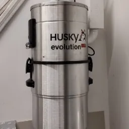 Zamontowany centralny odkurzacz Husky Evolution ze srebrną obudową w pomieszczeniu z białymi ścianami i widoczną instalacją elektryczną.