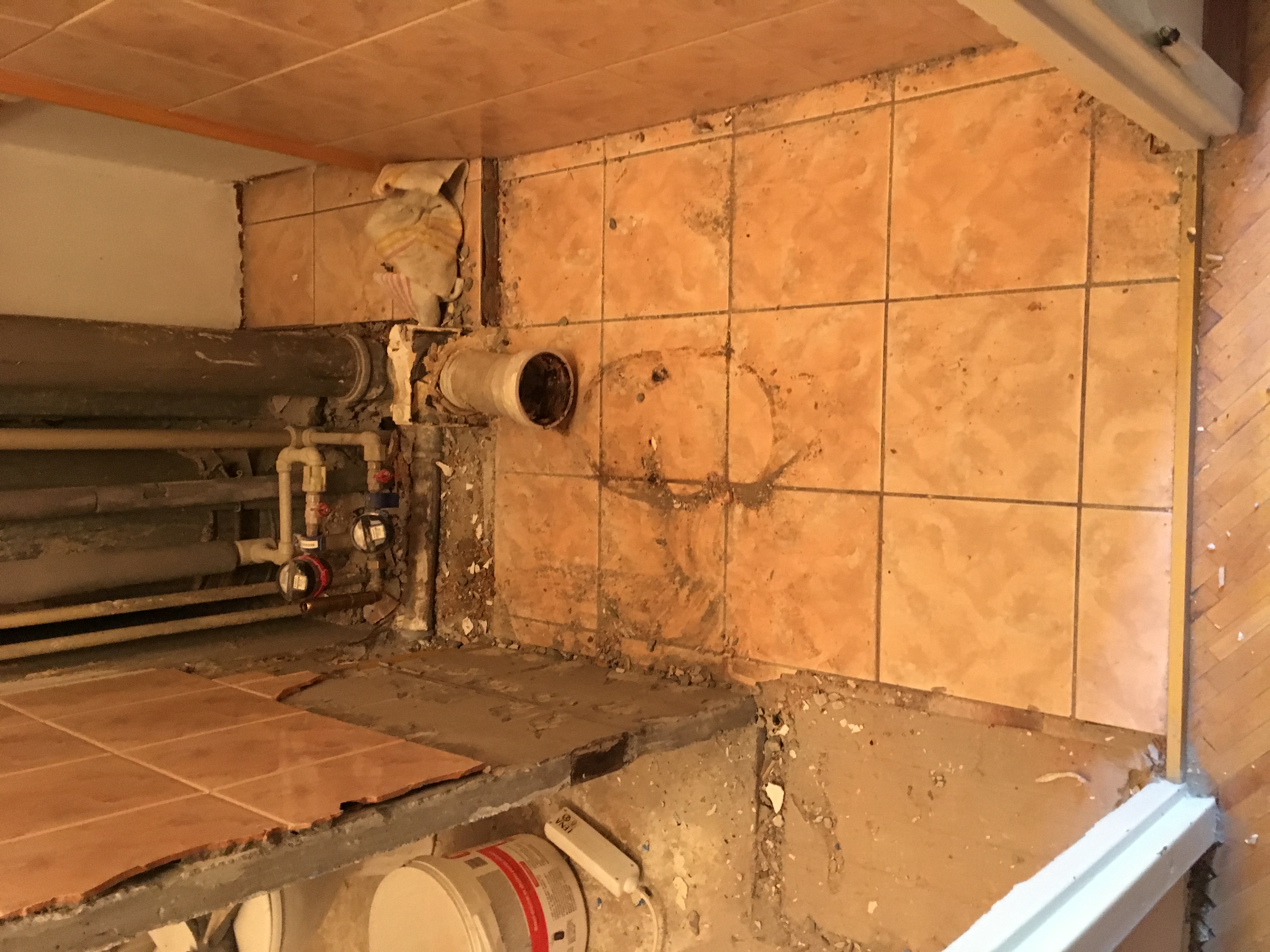 Demontaż starej glazury we Wrocławiu, widoczne odsłonięte rury, resztki kleju i gruzu, przygotowanie do położenia nowych płytek.