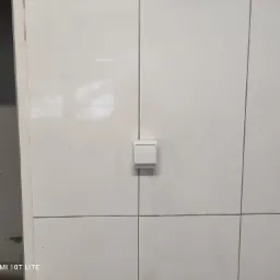 Biały włącznik światła zamontowany na białej, kafelkowanej ścianie w nowym budynku, widoczne fugi.