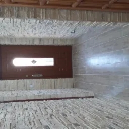 Wykończone wnętrze: Ściany i podłoga wyłożone płytkami imitującymi kamień, drewniana stolarka drzwiowa z dekoracyjnym przeszkleniem, widoczne przewody elektryczne.