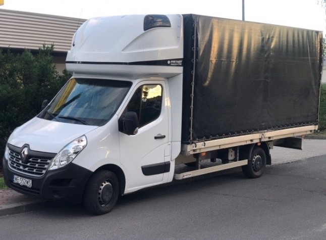 Biały samochód dostawczy Renault Master z czarną plandeką na pace, zaparkowany na ulicy, widoczny z boku, z numerem rejestracyjnym WE 552WS.
