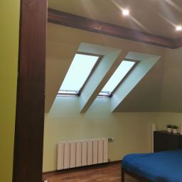 HelpHend - Poddasze w Olszewnicy Starej z dwoma oknami dachowymi, świeżo pomalowane na jasnozielony kolor, drewniana podłoga i niebieska pościel na łóżku.