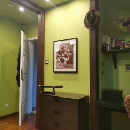 HelpHend - Jasnozielony pokój z drewnianymi belkami, komodą z mieczem samurajskim, obrazem na ścianie, otwartymi drzwiami i półką z książkami i trofeami myśliwskimi.