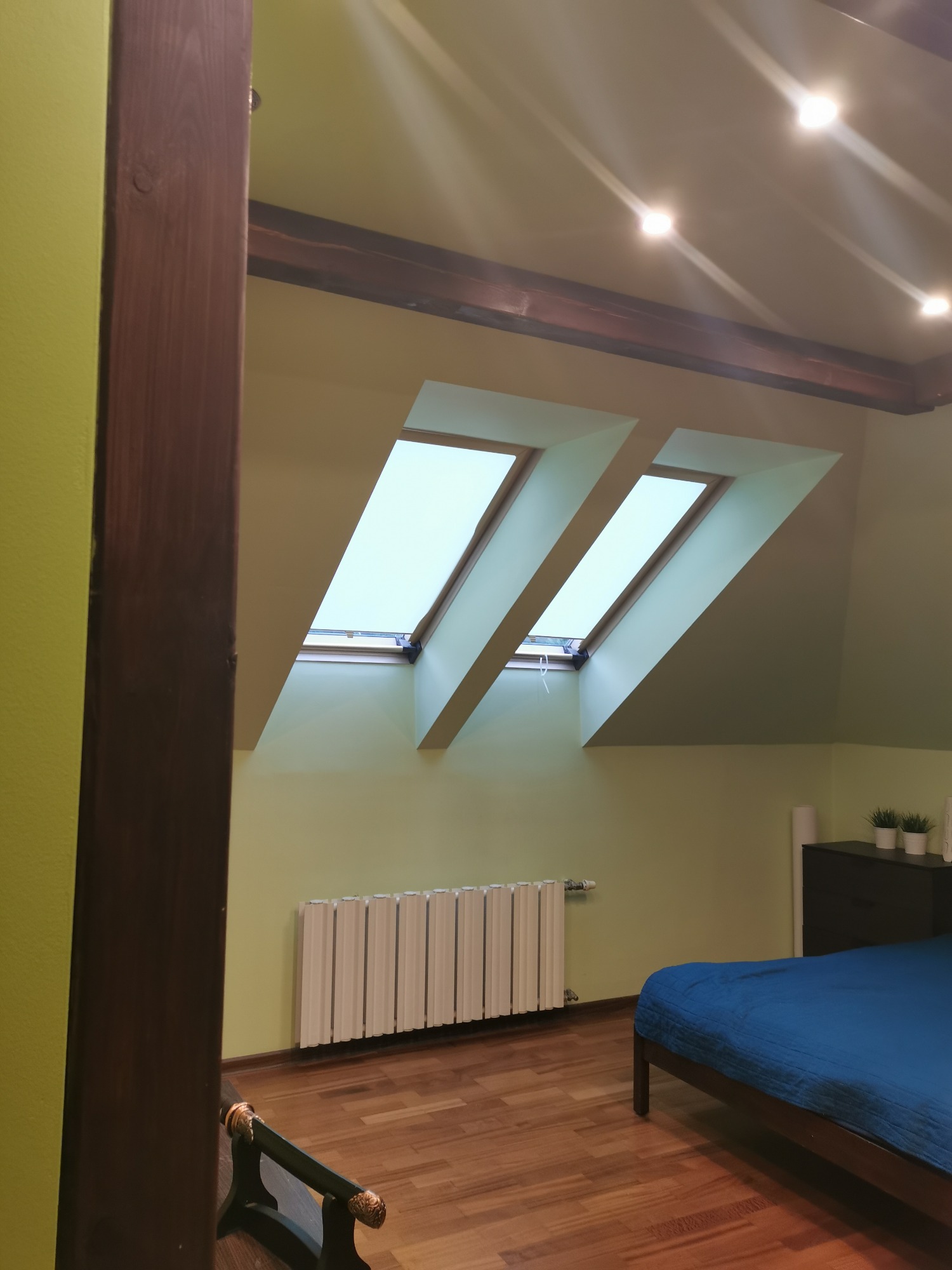 Poddasze w Olszewnicy Starej z dwoma oknami dachowymi, świeżo pomalowane na jasnozielony kolor, drewniana podłoga i niebieska pościel na łóżku.