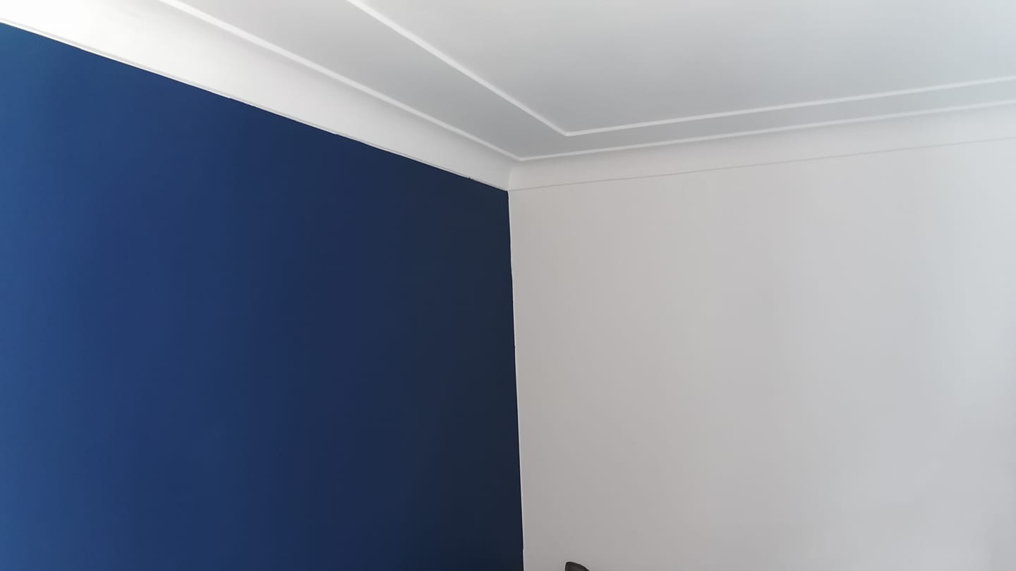 Pomieszczenie po remoncie: ściana pomalowana na granatowo kontrastuje z białą ścianą i listwami przysufitowymi.