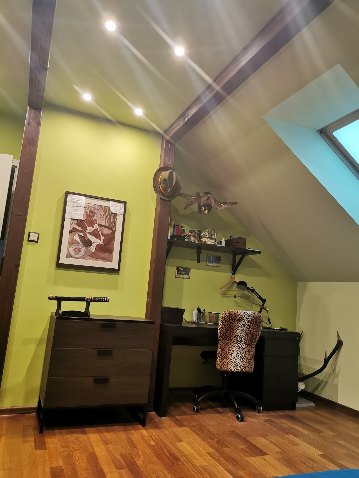 Poddasze zaadaptowane na gabinet z drewnianymi belkami, biurkiem, komodą z kataną, krzesłem w panterkę i oknem dachowym.