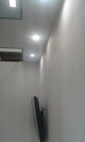 Świeżo pomalowane, białe ściany z zamontowanym telewizorem i punktowym oświetleniem sufitowym