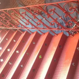 Czerwone, metalowe schody z ozdobną balustradą, widok z góry, schody z wytłoczonym wzorem i wyciętymi otworami w kształcie koniczyny.