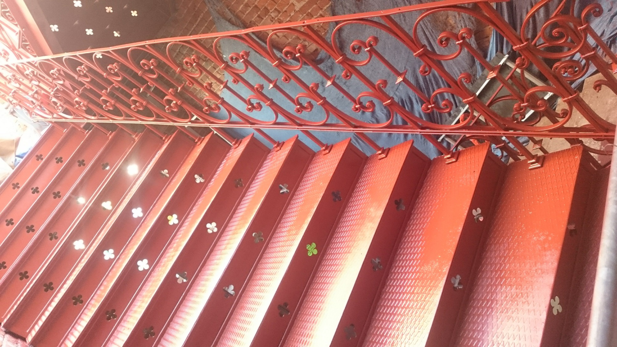 Czerwone, metalowe schody z ozdobną balustradą, widok z góry, schody z wytłoczonym wzorem i wyciętymi otworami w kształcie koniczyny.