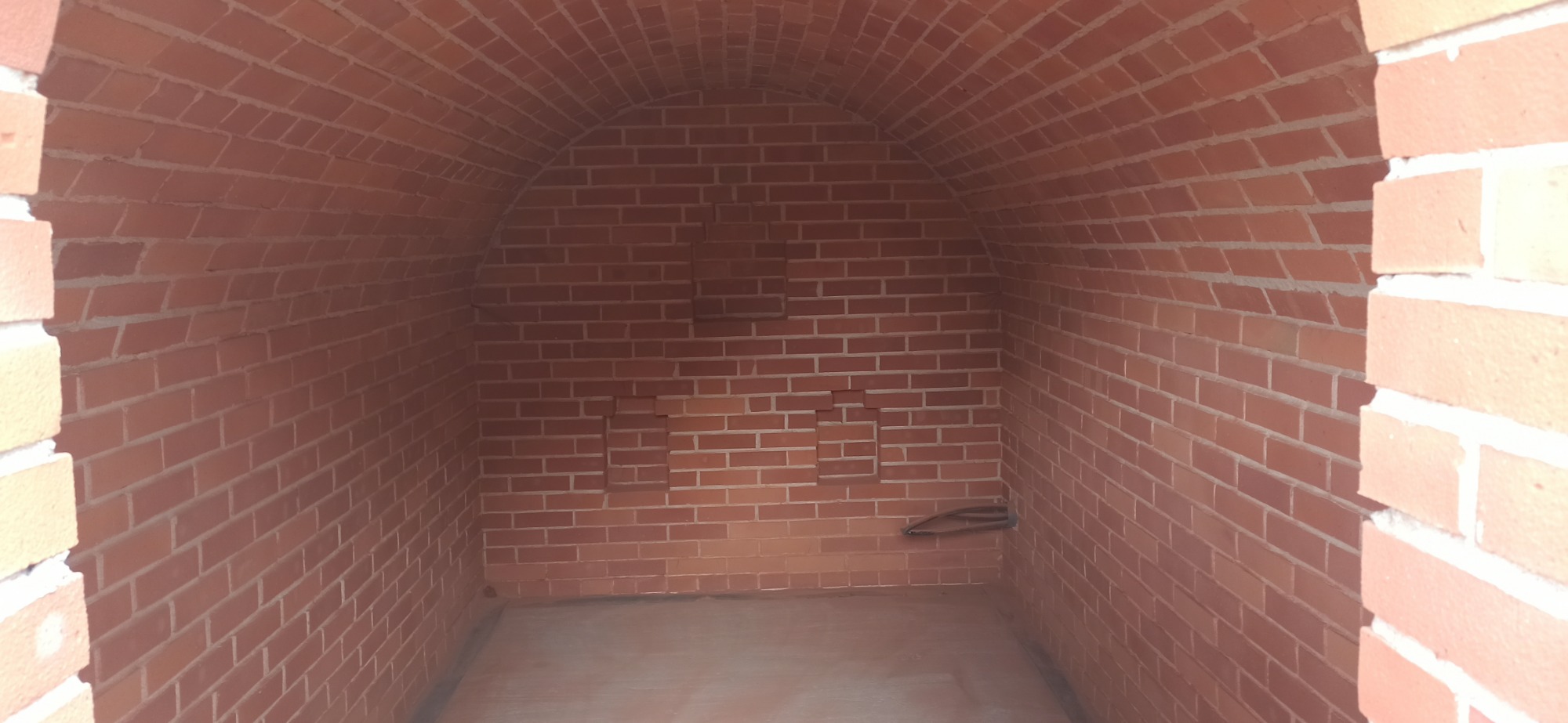 Wnętrze pieca chlebowego z czerwonej cegły, z łukowatym sklepieniem i wnęką na narzędzia, widok z przodu.
