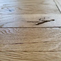 Fragment wycyklinowanej, jasnej podłogi drewnianej z wyraźnym usłojeniem i naturalnym sękiem w desce, sfotografowany pod niskim kątem.