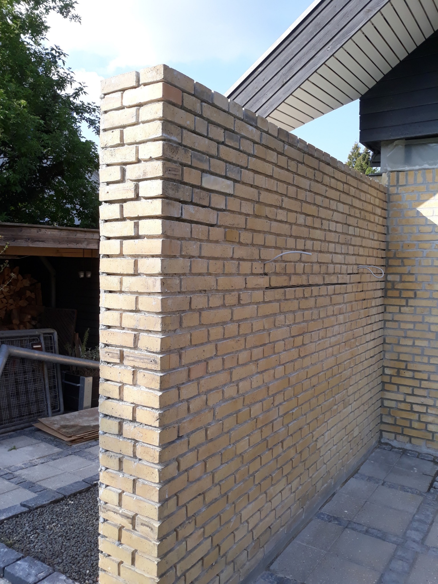 Żółta ściana z cegły klinkierowej, częściowo wykończona, z widocznymi przewodami instalacji elektrycznej, na zewnątrz budynku.