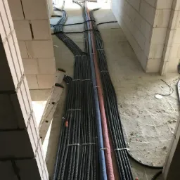 Instalacja przewodów elektrycznych w peszlach i rur w surowym stanie budynku, widoczna drabina aluminiowa i białe ściany z betonu komórkowego.