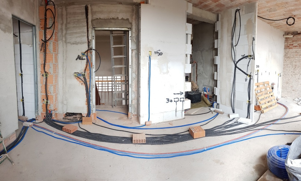 Rozprowadzenie przewodów elektrycznych i rur instalacyjnych w surowym wnętrzu w Krakowie, widoczne ściany w trakcie budowy i cegły podtrzymujące przewody.