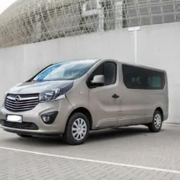 Szary Opel Vivaro Tourer zaparkowany na parkingu z widokiem na Stadion Miejski we Wrocławiu, prezentujący przestronność i komfort przewozu osób.