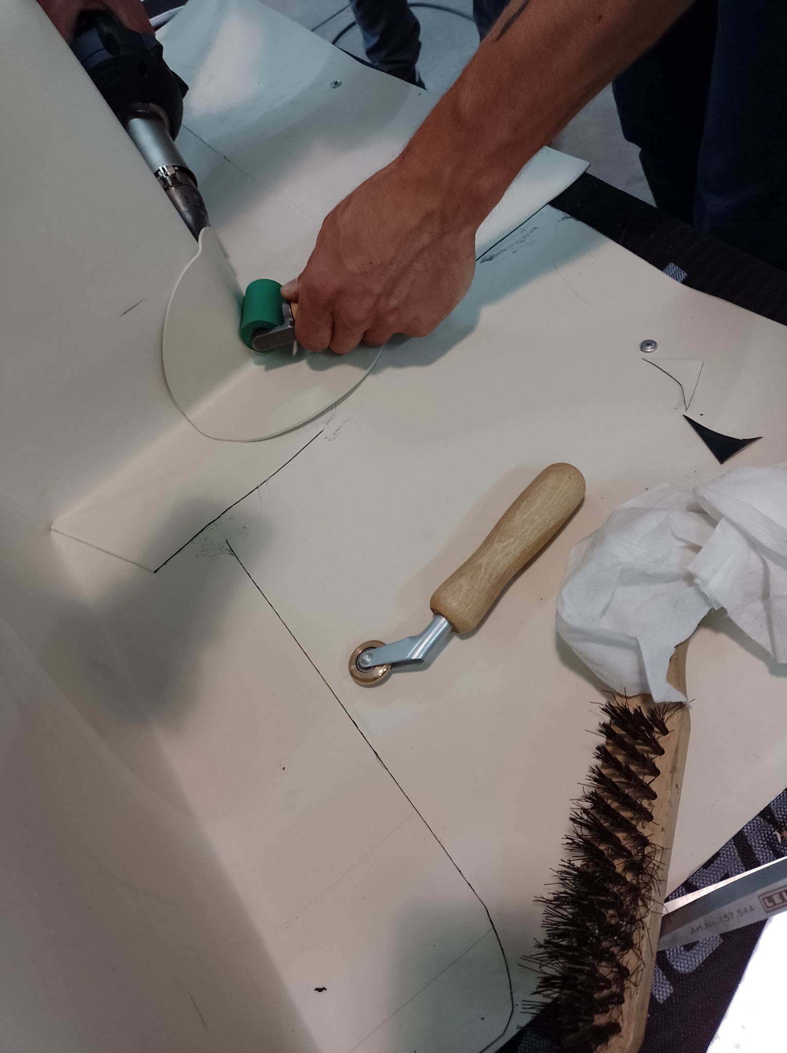 Prace dekarskie: Zgrzewanie membrany dachowej za pomocą zgrzewarki i dociskanie wałkiem, widoczne narzędzia dekarskie i szczotka do czyszczenia.