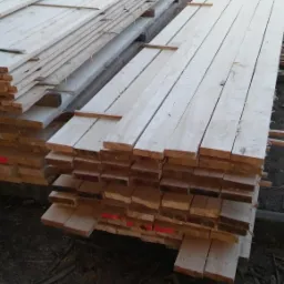 Stosy jasnej tarcicy ułożone na zewnątrz, z wózkiem widłowym w tle.