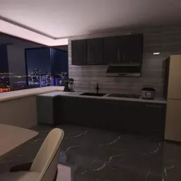 Wizualizacja nowoczesnej kuchni z widokiem na nocne miasto, ciemne szafki, marmurowa podłoga, stół z owocami.