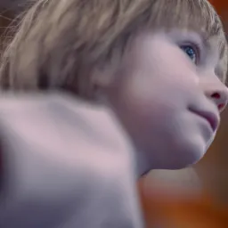 Portret z profilu dziecka z Zgorzelca z blond włosami i niebieskimi oczami, spoglądającego w górę na rozmytym, kolorowym tle.