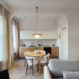 Kania Design Dorota Orlińska-Kania - Jasne wnętrze mieszkania z okrągłym stołem i krzesłami, widok na kuchnię z białymi szafkami i drewnianymi blatami. Minimalistyczny design, parkiet w jodełkę.