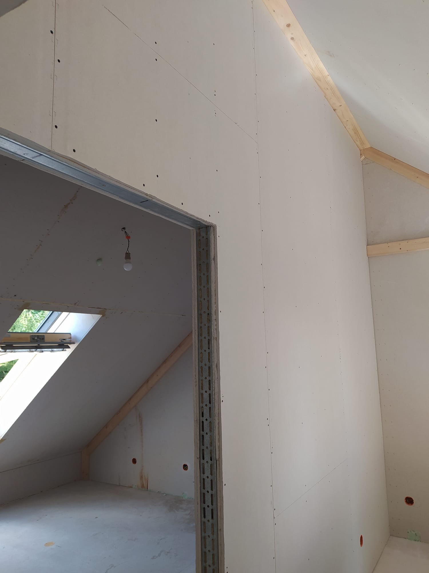 Montaż płyt na poddaszu z widocznymi elementami konstrukcji drewnianej dachu i metalową ramą drzwiową.