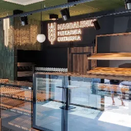 Nowoczesne wnętrze piekarni-cukierni 'Magdalenka' w Łodzi: zielone płytki na ścianie, neonowy szyld, drewniane regały i przeszklone witryny ekspozycyjne.