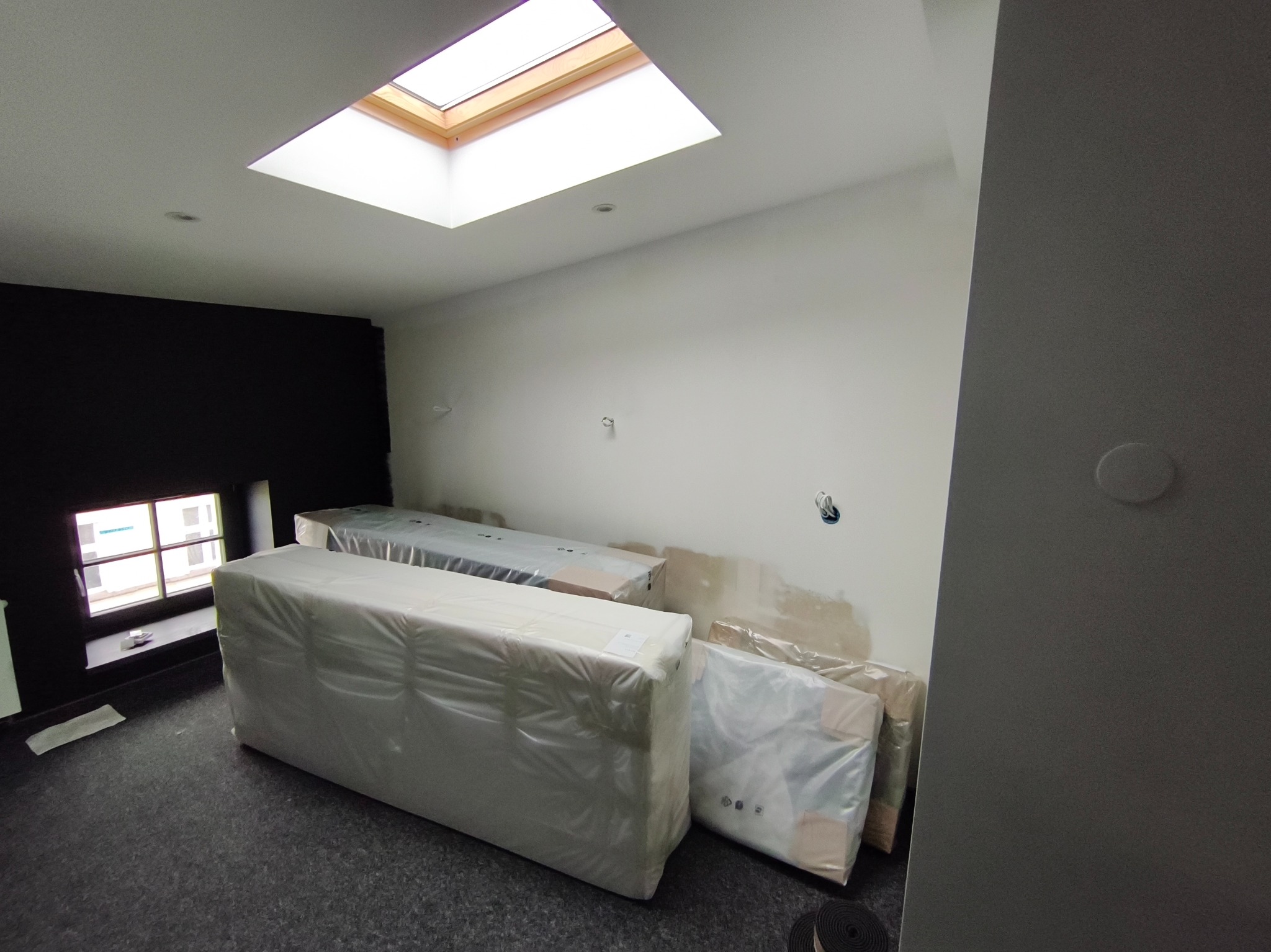 Nowe wyposażenie łazienki w folii ochronnej, przygotowane do montażu w Łodzi. Widoczne wnęki instalacyjne i okno dachowe.