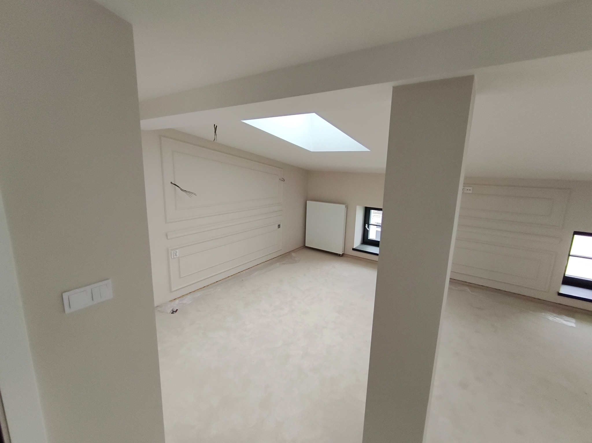 Jasne, przestronne wnętrze po remoncie z dekoracyjnymi panelami ściennymi i oknem dachowym. Widoczne przygotowania do dalszych prac wykończeniowych.