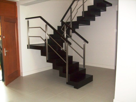 Nowoczesne, ciemne schody z metalowymi balustradami w minimalistycznym wnętrzu, widoczne z poziomu dolnego biegu, z otwartymi drzwiami po lewej stronie.