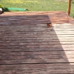 Świeżo pomalowany drewniany taras z widokiem na jezioro, puszka z farbą i pędzel obok