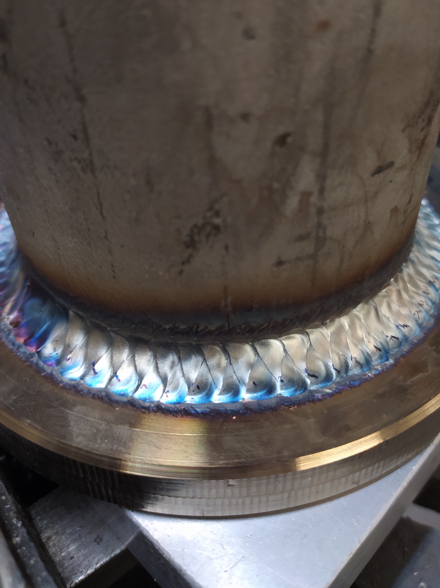 Detal spoiny na rurze ze stali nierdzewnej, widoczne tęczowe przebarwienia termiczne i precyzyjne ułożenie spawów.